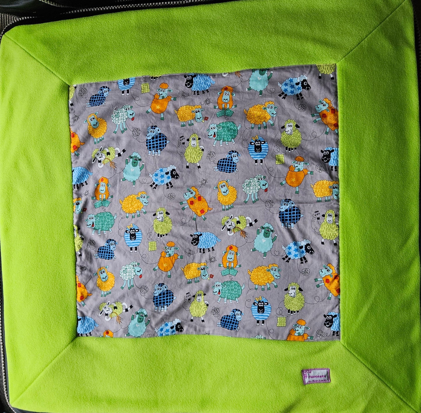 Fun Colourful Sheep's Handmade Blanket on Grey background. Double sided, cotton fabric in one side, and bright fluorescent green fleece at the back.